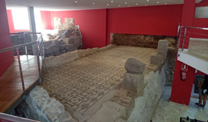 Junto al portal de un edificio moderno y elevado, se accede a los bajos de éste: una casa romana